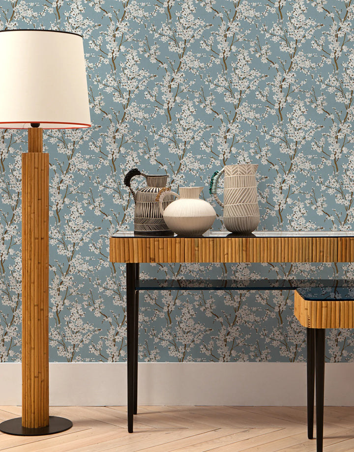 Hellblaue Japandi Vliestapete mit weißen Kirschblütenzweigen im Wohnzimmer
